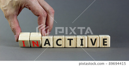 Active or inactive symbol. Businessman turns wooden cubes and changes the word Inactive to Active. Beautiful grey table grey background, copy space. Business and active or inactive concept. 89694415