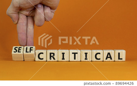 Critical or self-critical symbol. Wooden cubes with words Self-critical or critical. Businessman hand. Beautiful orange background. Psychology, critical or self-critical business concept. Copy space. 89694426