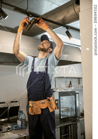 Male worker fixing ceiling lamp in cafe 89694502