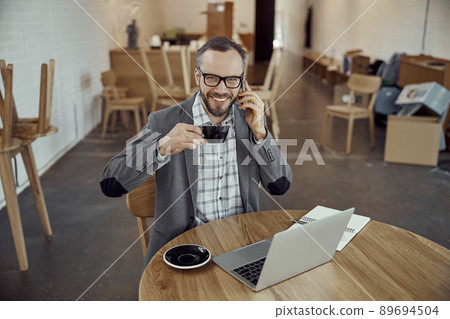 Cheerful man drinking coffee and talking on cellphone in cafe 89694504