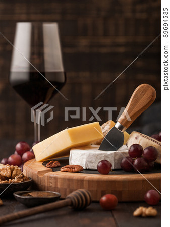 Glass of red wine with selection of various cheese on the board and grapes on wooden table 89694585