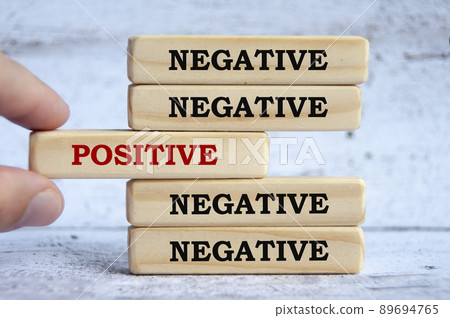 Negative and positive text on wooden blocks with hand placing a wooden block in the middle. Negative and positive text on wooden blocks with hand placing a wooden block in the middle. 89694765