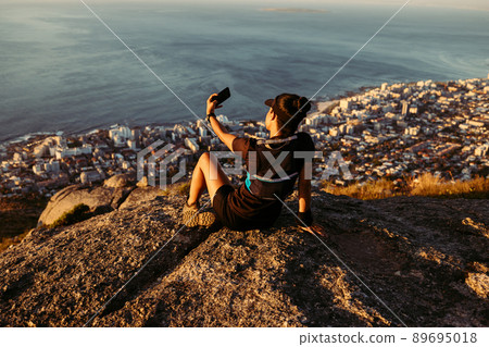 Woman in sportswear standing on the cliff and looking at the view at sunset. Female trail runner relaxing on mountain top looking at the ocean. Woman in sportswear standing on the cliff and looking at the view at sunset. Female trail runner relaxing on mountain top looking at the ocean. 89695018