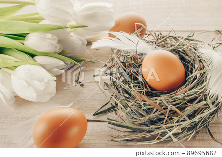 Easter eggs nature. Natural colour egg in basket with spring tulips, white feathers on wooden table background in Happy Easter decoration. Congratulatory easter design. Easter eggs nature. Natural colour egg in basket with spring tulips, white feathers on wooden table background in Happy Easter decoration. Congratulatory easter design. 89695682