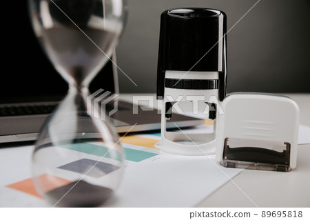 Office desk table with laptop, hourglass and rubber stamp. Concept of contract, consent, clerk working in the office Office desk table with laptop, hourglass and rubber stamp. Concept of contract, consent, clerk working in the office 89695818