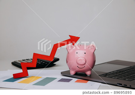 Pink piggy bank and red arrow up graphic in office Pink piggy bank and red arrow up graphic in office 89695893