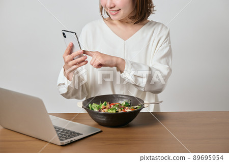 A young vegan woman eating oatmeal while looking at her smartphone 89695954