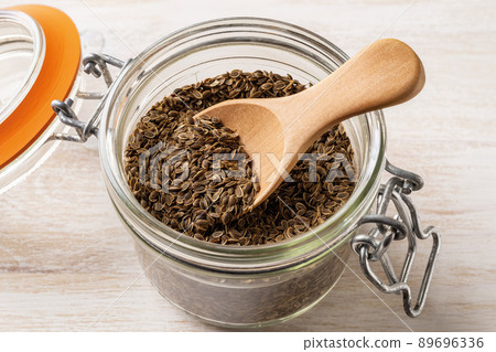 Whole dill seeds and wooden spoon in a clip top glass jar close-up. 89696336