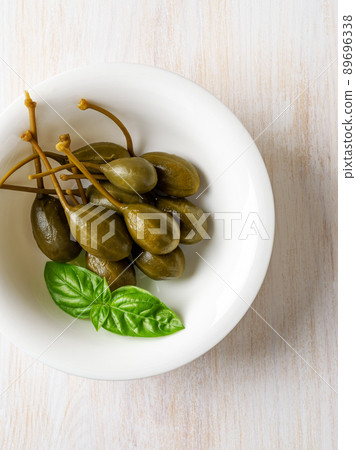 Pickled caper fruits and fresh basil leaf in a white bowl on a rustic table. 89696338
