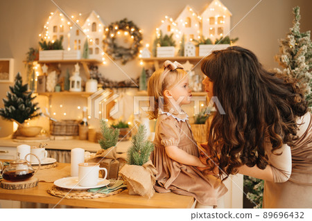 mom and pretty little girl at the kitchen table. beautiful new year's interior mom and pretty little girl at the kitchen table. beautiful new year's interior 89696432