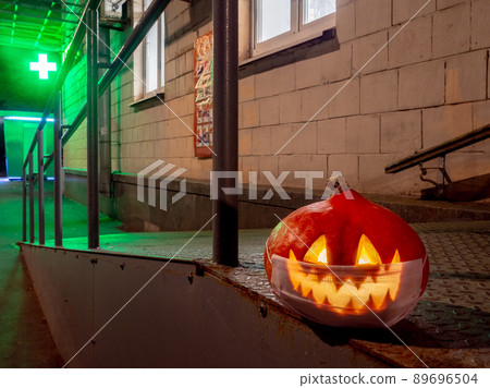 Halloween pumpkin at night against the background of a pharmacy cross glowing in the dark. 89696504