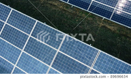 Aerial drone view flight over solar panels on sunny day close-up. Photovoltaic solar panel. Moving over solar panels with sun glare. Production of renewable alternative energy. Green ecological energy Aerial drone view flight over solar panels on sunny day close-up. Photovoltaic solar panel. Moving over solar panels with sun glare. Production of renewable alternative energy. Green ecological energy 89696634