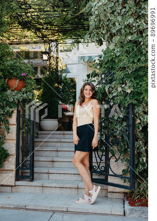 Girl Tourist Walking Through Ancient Narrow Street On A Beautiful Summer Day In MEDITERRANEAN MEDIEVAL CITY, OLD TOWN BUDVA, MONTENEGRO. Young Beautiful Cheerful Woman Walking On Old Street At Girl Tourist Walking Through Ancient Narrow Street On A Beautiful Summer Day In MEDITERRANEAN MEDIEVAL CITY, OLD TOWN BUDVA, MONTENEGRO. Young Beautiful Cheerful Woman Walking On Old Street At 89696991
