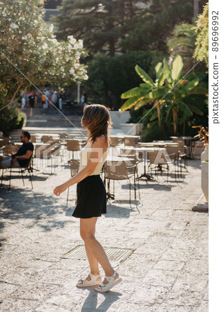 Girl Tourist Walking Through Ancient Narrow Street On A Beautiful Summer Day In MEDITERRANEAN MEDIEVAL CITY, OLD TOWN BUDVA, MONTENEGRO. Young Beautiful Cheerful Woman Walking On Old Street At Girl Tourist Walking Through Ancient Narrow Street On A Beautiful Summer Day In MEDITERRANEAN MEDIEVAL CITY, OLD TOWN BUDVA, MONTENEGRO. Young Beautiful Cheerful Woman Walking On Old Street At 89696992