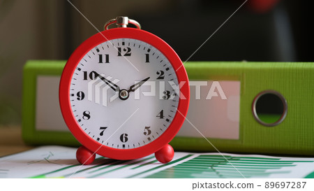 Red alarm clock with financial business charts and documents on table 89697287