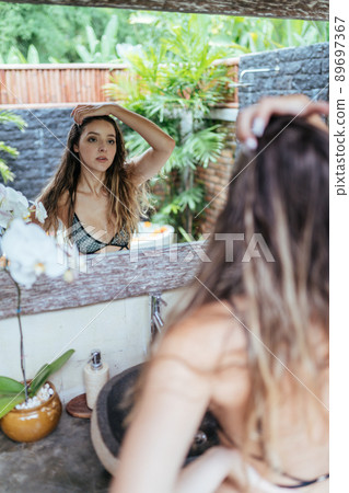 very carefully examines in the mirror her face beautiful girl in a swimsuit very carefully examines in the mirror her face beautiful girl in a swimsuit 89697367