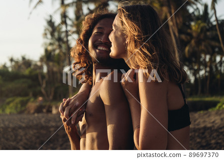 A loving couple against a background of palm trees and sand stand in a hug and smile at each other man and woman A loving couple against a background of palm trees and sand stand in a hug and smile at each other man and woman 89697370