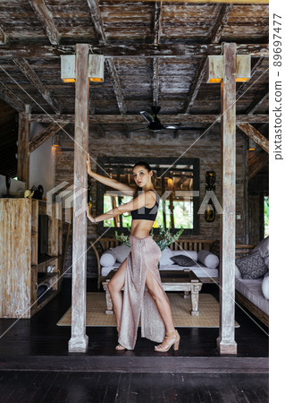 In the interior hold the ceiling two wooden columns between them stands leaning on one hand girl in a skirt with a cut and top In the interior hold the ceiling two wooden columns between them stands leaning on one hand girl in a skirt with a cut and top 89697477