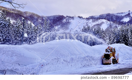 A landscape where a snowplow during snow removal work blows snow out 89698777