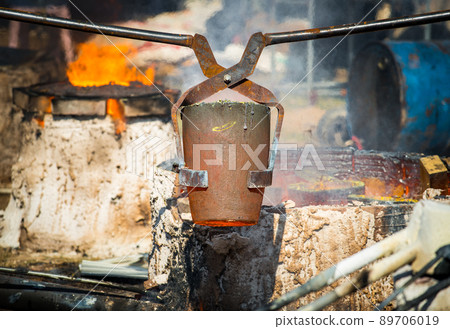 Shot of Thai blacksmith holding a hot crucible by the iron pliers from furnace. Gold melting process with gasoline burner in crucible. Shot of Thai blacksmith holding a hot crucible by the iron pliers from furnace. Gold melting process with gasoline burner in crucible. 89706019