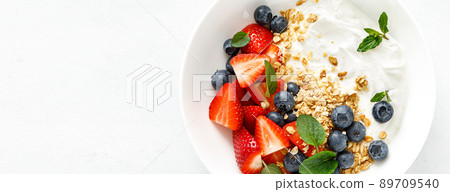 Breakfast bowl with granola, plain yogurt, strawberry and blueberry. Top view. Banner 89709540