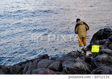 An angler fishing on a rough shore created by a lava flow An angler fishing on a rough shore created by a lava flow 89712110