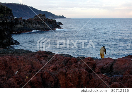 An angler fishing on a rough shore created by a lava flow 89712116