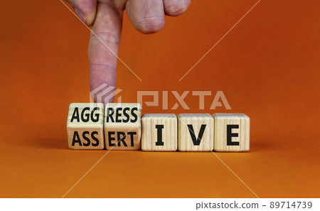 Aggressive or assertive symbol. Businessman turns wooden cubes, changes the word Aggressive to Assertive. Beautiful orange background, copy space. Business, psychological aggressive assertive concept. Aggressive or assertive symbol. Businessman turns wooden cubes, changes the word Aggressive to Assertive. Beautiful orange background, copy space. Business, psychological aggressive assertive concept. 89714739