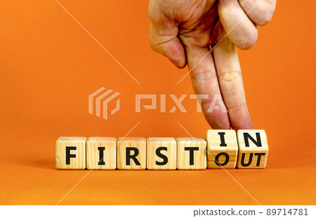 First in first out symbol. Businessman turns wooden cubes and changes words first in to first out. Beautiful orange table, orange background. Business and first in and out concept. Copy space. 89714781