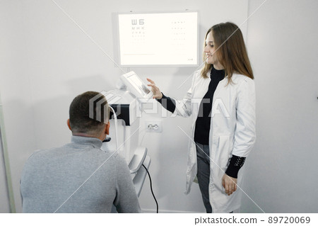Man checking up her sight at ophthalmology center. Female optometrist doing sight testing. Man wearing grey shirt. 89720069