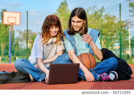 Friends students sitting on school basketball court looking at laptop 89721895