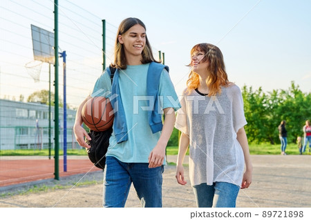 Young teenage male female students with ball walking outdoor near basketball court Young teenage male female students with ball walking outdoor near basketball court 89721898
