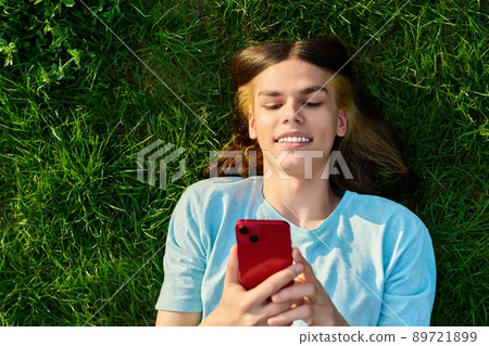 Young guy with smartphone in his hands on green grassy background Young guy with smartphone in his hands on green grassy background 89721899