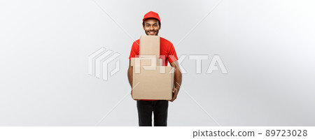 Delivery Concept - Portrait of Happy African American delivery man in red cloth holding a box package. Isolated on Grey studio Background. Copy Space. 89723028