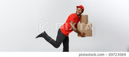Delivery Concept - Handsome African American delivery man rush running for delivering a package for customer. Isolated on Grey studio Background. Copy Space. Delivery Concept - Handsome African American delivery man rush running for delivering a package for customer. Isolated on Grey studio Background. Copy Space. 89723069