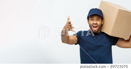 Delivery Concept - Portrait of Serious African American delivery man showing silly aggressive expression with holding a box package. Isolated on Grey studio Background. Copy Space. 89723070