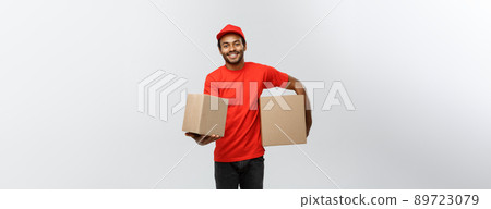 Delivery Concept - Portrait of Happy African American delivery man in red cloth holding a box package. Isolated on Grey studio Background. Copy Space. 89723079