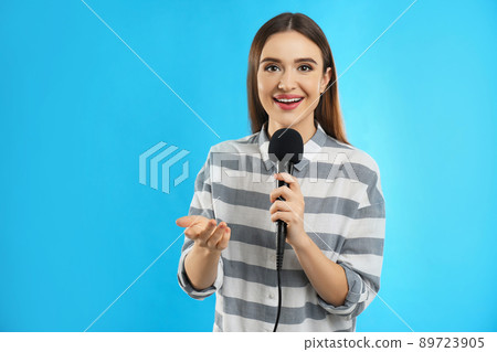 Young female journalist with microphone on blue background Young female journalist with microphone on blue background 89723905