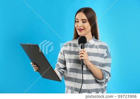 Young female journalist with microphone and clipboard on blue background Young female journalist with microphone and clipboard on blue background 89723906