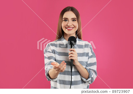 Young female journalist with microphone on pink background 89723907