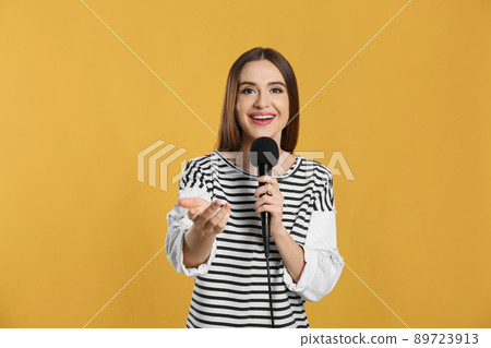 Young female journalist with microphone on yellow background 89723913
