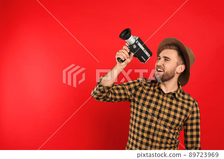 Young man with vintage video camera on red background. Space for text 89723969