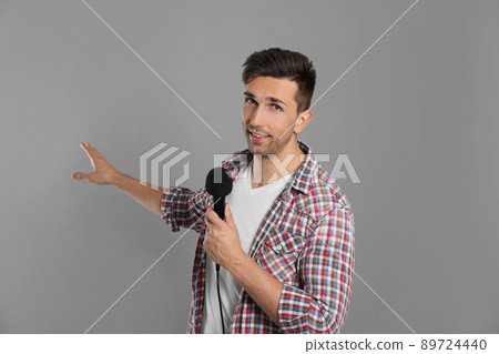 Young male journalist with microphone on grey background Young male journalist with microphone on grey background 89724440
