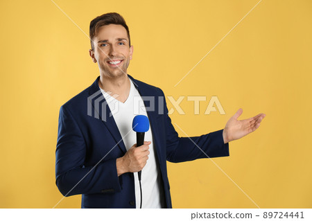 Young male journalist with microphone on yellow background Young male journalist with microphone on yellow background 89724441