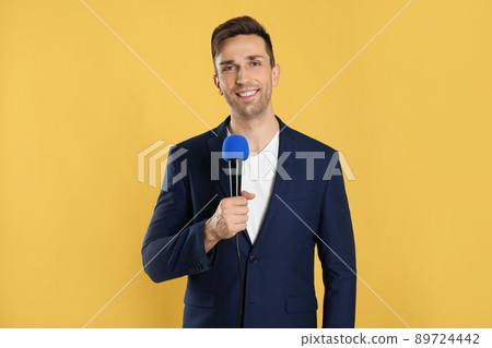 Young male journalist with microphone on yellow background Young male journalist with microphone on yellow background 89724442