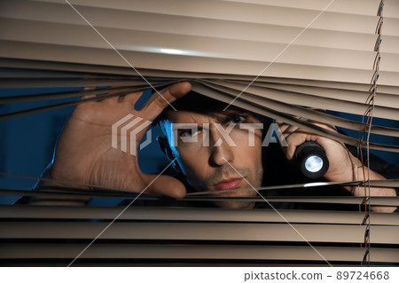 Male security guard with flashlight looking through window blinds in darkness Male security guard with flashlight looking through window blinds in darkness 89724668
