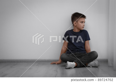 Sad little boy sitting on floor indoors, space for text. Child in danger 89724702