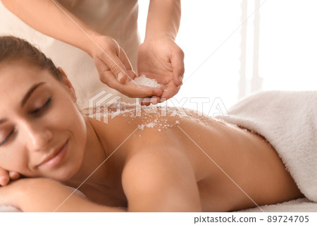 Young woman having body scrubbing procedure with sea salt in spa salon 89724705