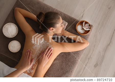 Young woman having body scrubbing procedure with sea salt in spa salon, top view 89724710