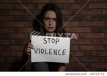 Abused young woman with sign STOP VIOLENCE near brick wall 89724718